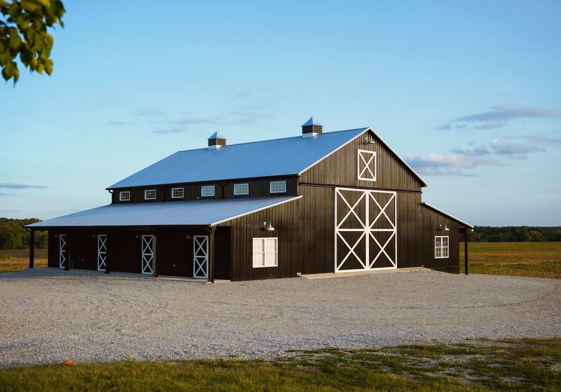 Black barn with white trim, metal roof, and large sliding doors in a rural landscape, ideal for agricultural storage or events, showcasing quality construction and versatile design.
